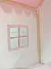 Pink play tent with a square window and wooden frame.